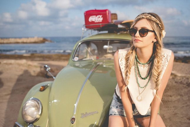 Kobieta w stylizacji retro siedzi przy klasycznym samochodzie na plaży