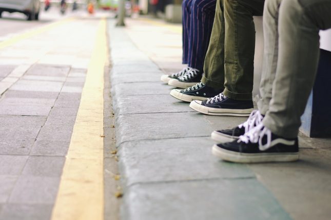 Nogi trzech osób w szerokich spodniach i trampkach siedzących na krawężniku